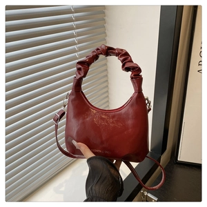 Detail of red glossy cloud-handle handbag with adjustable strap and textured finish