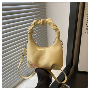 Detail of light yellow crescent handbag with ruched handle and glossy patent finish