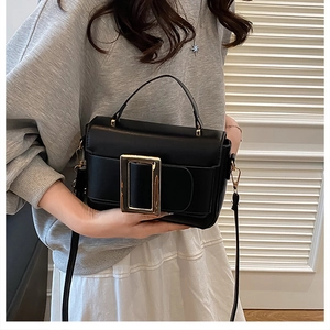 Detail of a black square crossbody bag featuring a prominent golden metallic buckle closure