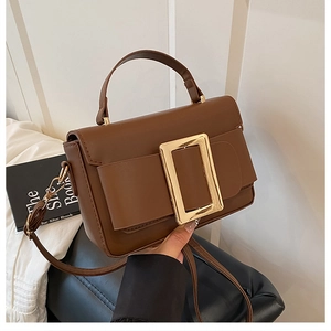 Detail of deep caramel square handbag featuring a large gold buckle and matte leather texture