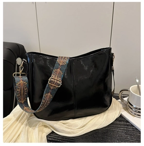Close-up of black glossy shoulder bag with a colorful ethnic pattern wide woven strap