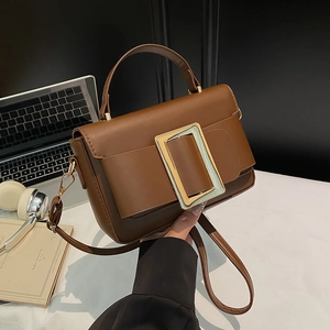 Classic brown rectangular shoulder bag with large gold buckle in a workplace setting
