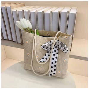 Detail of woven tote bag with white daisy embroidery and black polka dot scarf