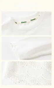 Detail of white cotton girl shirt featuring delicate lace embroidery on hem and cuffs