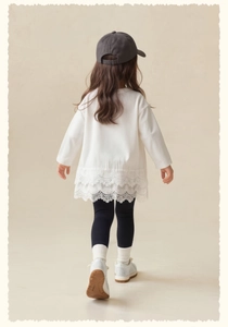 Detailed back view of girls' white long-sleeved shirt with elegant lace hem and black leggings