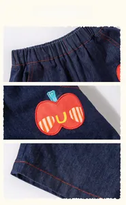 Detail of kids denim shorts with elastic waist, red stitching, and apple embroidery