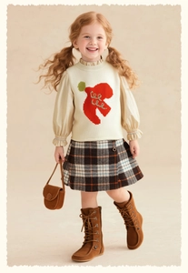 Détail de la broderie pomme rouge sur un gilet en tricot beige pour enfants