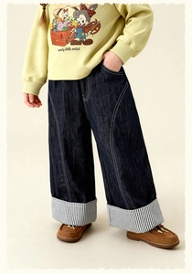Détail d'un jean bleu foncé pour filles avec surpiqûres blanches et revers à rayures noires
