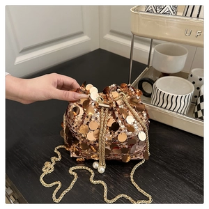 Detail view of gold sequin bucket bag featuring chain strap and pearl drawstring tassels