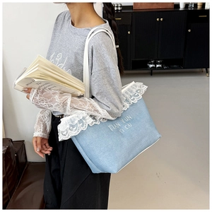 Gros plan d'un sac cabas bleu clair avec bordure en dentelle blanche et broderie
