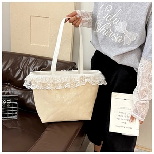 Detail of lace trim and embroidered logo on a large beige canvas commuter tote bag