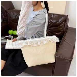 Detail of beige canvas tote bag featuring white lace trim and embroidered lettering