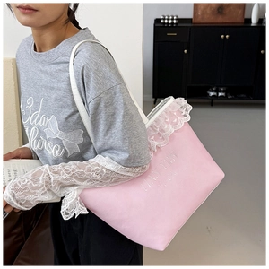 Detail of pink canvas tote bag with white lace trim and embroidered lettering on shoulder