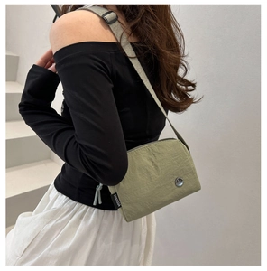 Détail d'un sac bandoulière en nylon vert herbe avec logo argenté et étiquette tissée