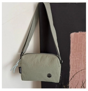 Detail view of the light green nylon mini crossbody bag with metal logo and woven strap