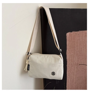 Detail of white nylon crossbody bag featuring a side brand label and metal logo
