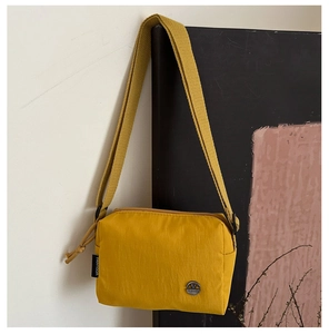 Close-up of yellow nylon crossbody bag featuring a metal M logo and adjustable strap