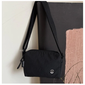 Detail of black nylon crossbody bag with woven strap and metallic M logo emblem