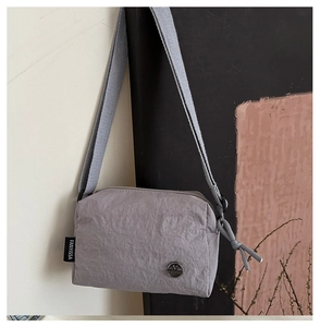 Close-up of light gray nylon crossbody bag showing the metallic logo and fabric texture