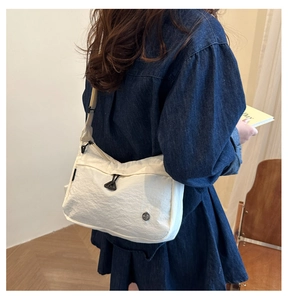 Detail of white nylon crossbody bag featuring an adjustable strap and drawstring front pocket