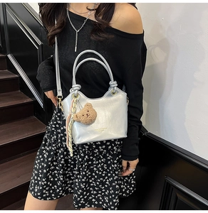Detail of silver metallic bucket bag featuring double ring handles and a plush bear charm
