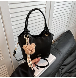 Detail of black tote bag with plush bear charm and gold lettering on premium PU leather