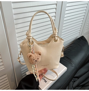 Detail of cream PU leather bucket bag with plush bear charm and metallic handle rings