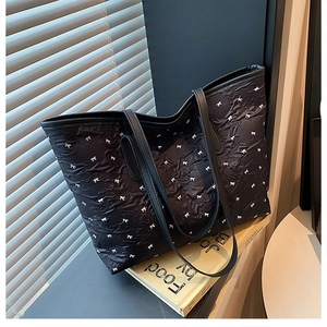 Detail der schwarzen Shopper-Tasche mit Schleifenmuster und Faltenstruktur auf Weiß