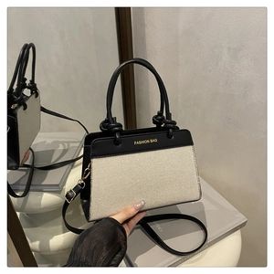 Detail of canvas handbag featuring black leather trim and knot-decorated top handle
