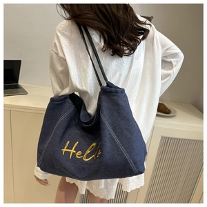 Gros plan de la broderie jaune 'Hello' sur la surface d'un sac cabas en denim bleu