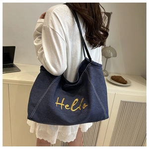 Detailed view of deep blue denim tote bag with yellow Hello embroidery and black straps