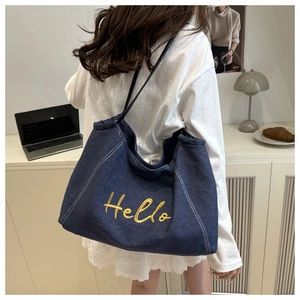 Detailed view of yellow Hello embroidery on blue denim tote bag with leather strap