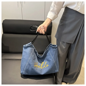 Détail du sac tote en denim bleu avec broderie Hello jaune et poignée en cuir noir