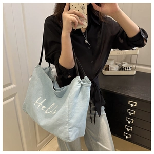 Détail du grand cabas en denim bleu clair avec broderie Hello porté par un mannequin
