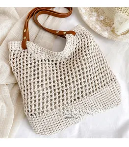 Dettaglio della borsa tote in paglia intrecciata con manici in pelle marrone e rivetti