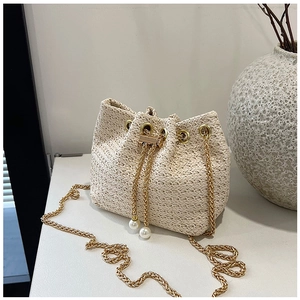 Detailed close-up of woven beige bucket bag featuring pearl charms and gold chain strap