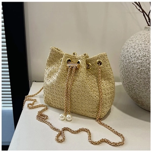 Detail of straw bucket bag featuring gold chain strap and pearl drawstring accents