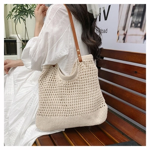 Outdoor shot of a woven hollow beach tote with brown leather straps on a wooden bench
