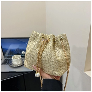 Macro detail of beige woven straw bucket bag featuring a gold chain and pearl drawstrings