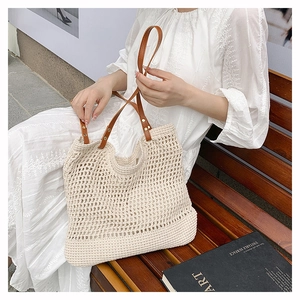 Detail of hollow-out mesh straw bag with brown leather strap and metal rivet design