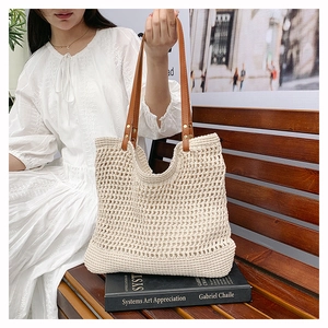 Hollow out woven straw tote bag with brown leather handles on a wooden bench scene