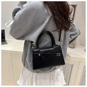 Detailed view of black mini crossbody bag with bow detail and buckle strap on model