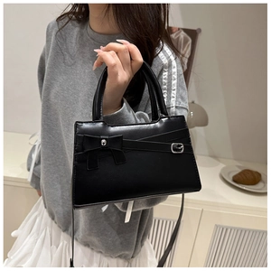 Detail of black bow handbag with silver buckle worn by model in a lifestyle setting