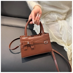 Detailed view of brown bowknot handbag with synthetic leather texture and shoulder strap
