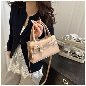Detail of apricot square handbag with bow accent and dual top handles held by model