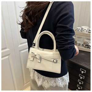 Detail of cream white crossbody bag with bow decoration shown on a model in a cozy room