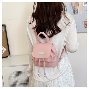Pink faux leather mini backpack with drawstring closure and bead detail shown on a model