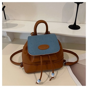 Detail of mini backpack featuring brown leather with blue denim flap and drawstring closure