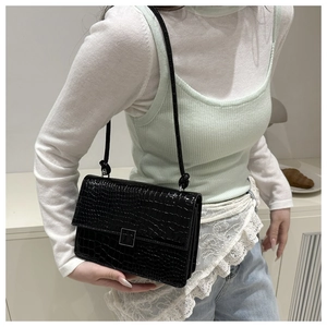 Detail of black crocodile pattern crossbody bag with square metal buckle on model
