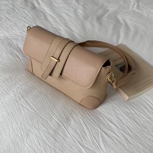 Sac baguette beige minimaliste avec texture tressée et boucle dorée sur tissu